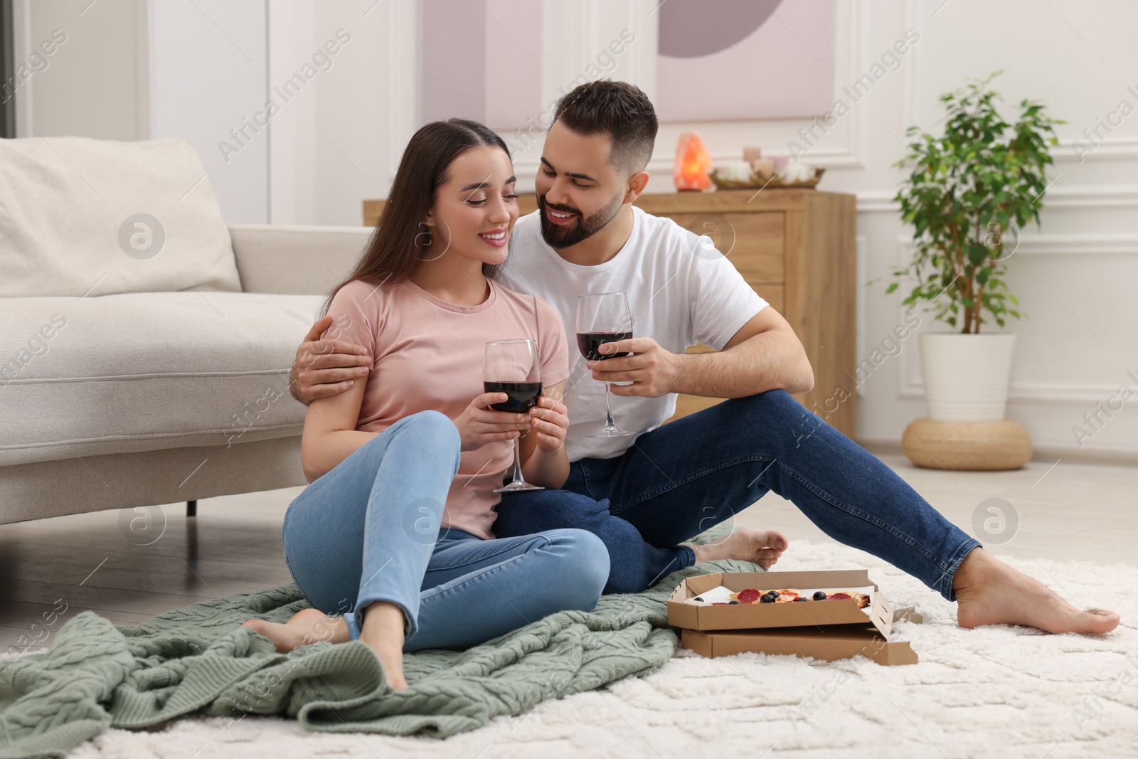 Photo of Affectionate young couple eating pizza and drinking wine at home