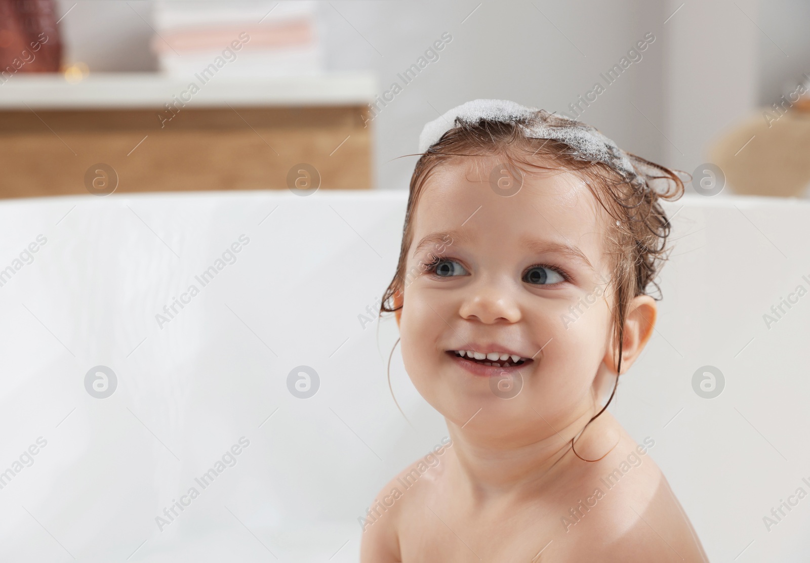 Photo of Cute little girl washing hair with shampoo in bathroom. Space for text