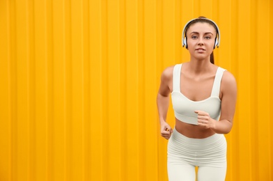 Young woman in sportswear with headphones  running near corrugated yellow metal wall. Space for text