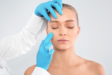 Doctor examining young woman face before cosmetic surgery on white background