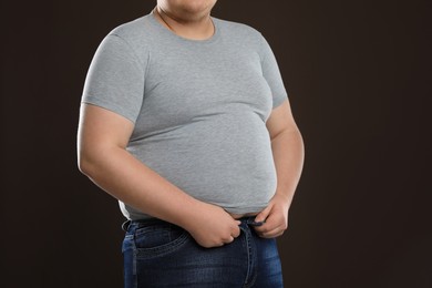 Photo of Overweight man trying to button up tight jeans on dark brown background, closeup