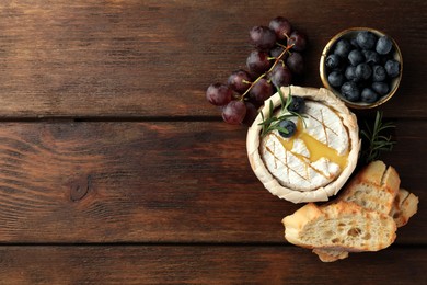 Tasty baked brie cheese and products on wooden table, flat lay. Space for text