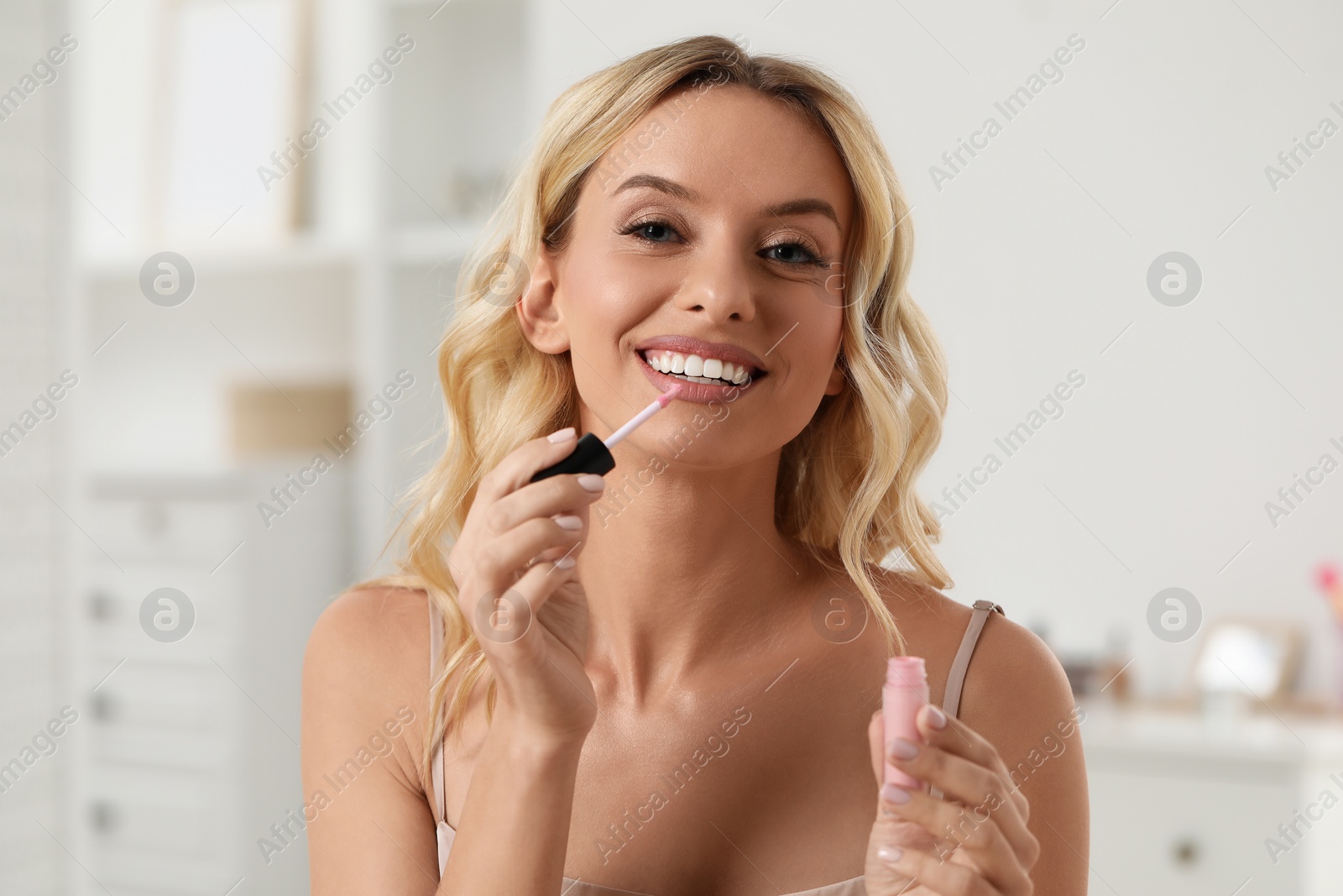 Photo of Beautiful makeup. Smiling woman applying liquid lipstick indoors