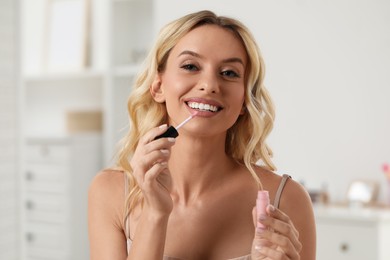 Beautiful makeup. Smiling woman applying liquid lipstick indoors