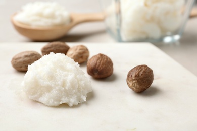 Photo of Shea butter and nuts on marble board, closeup. Space for text