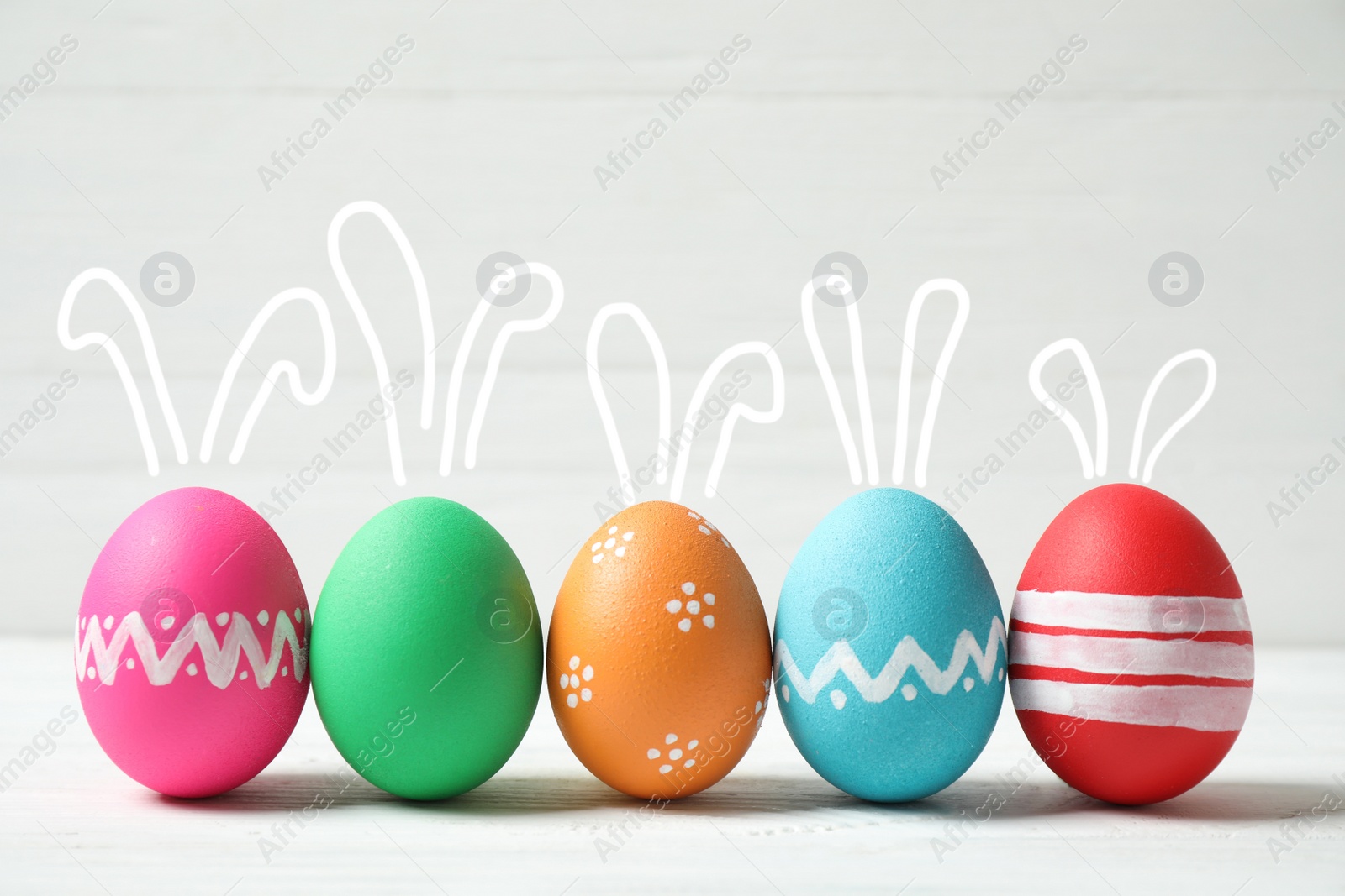 Image of Bright Easter eggs with cute bunny ears on white table