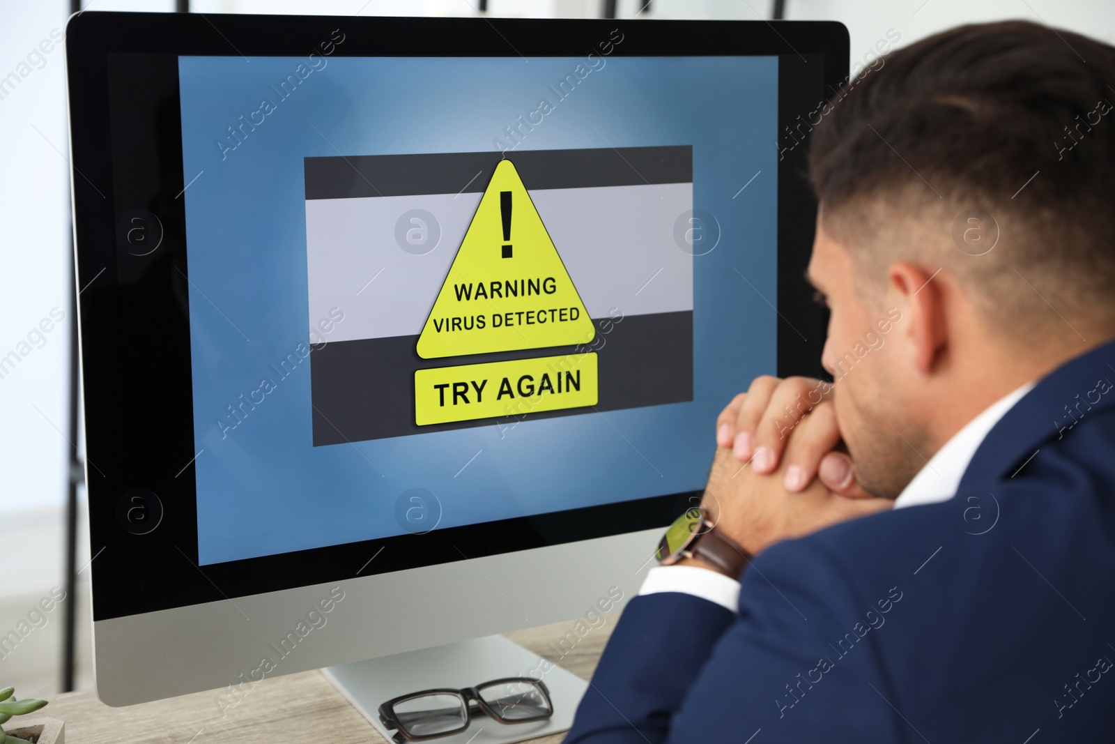 Photo of Office worker in front of computer with warning about virus attack on screen