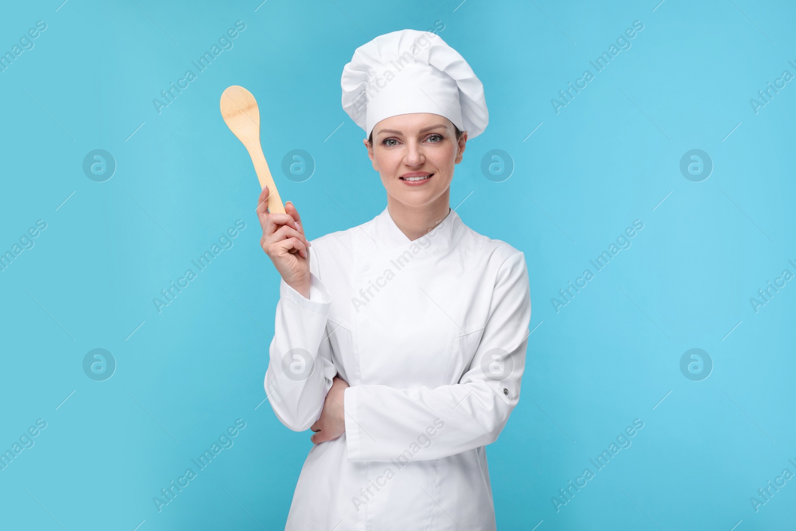 Photo of Happy woman chef in uniform holding wooden spoon on light blue background