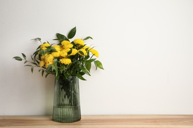 Photo of Bouquet of beautiful yellow flowers in glass vase on wooden table against white background. Space for text