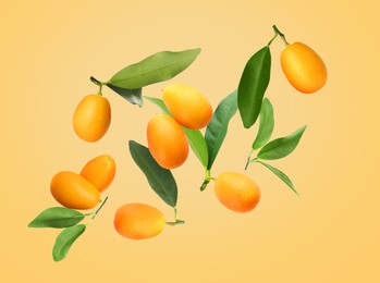 Image of Delicious fresh kumquats and green leaves falling on beige background