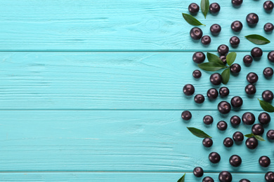 Fresh acai berries and green leaves on light blue wooden table, flat lay. Space for text