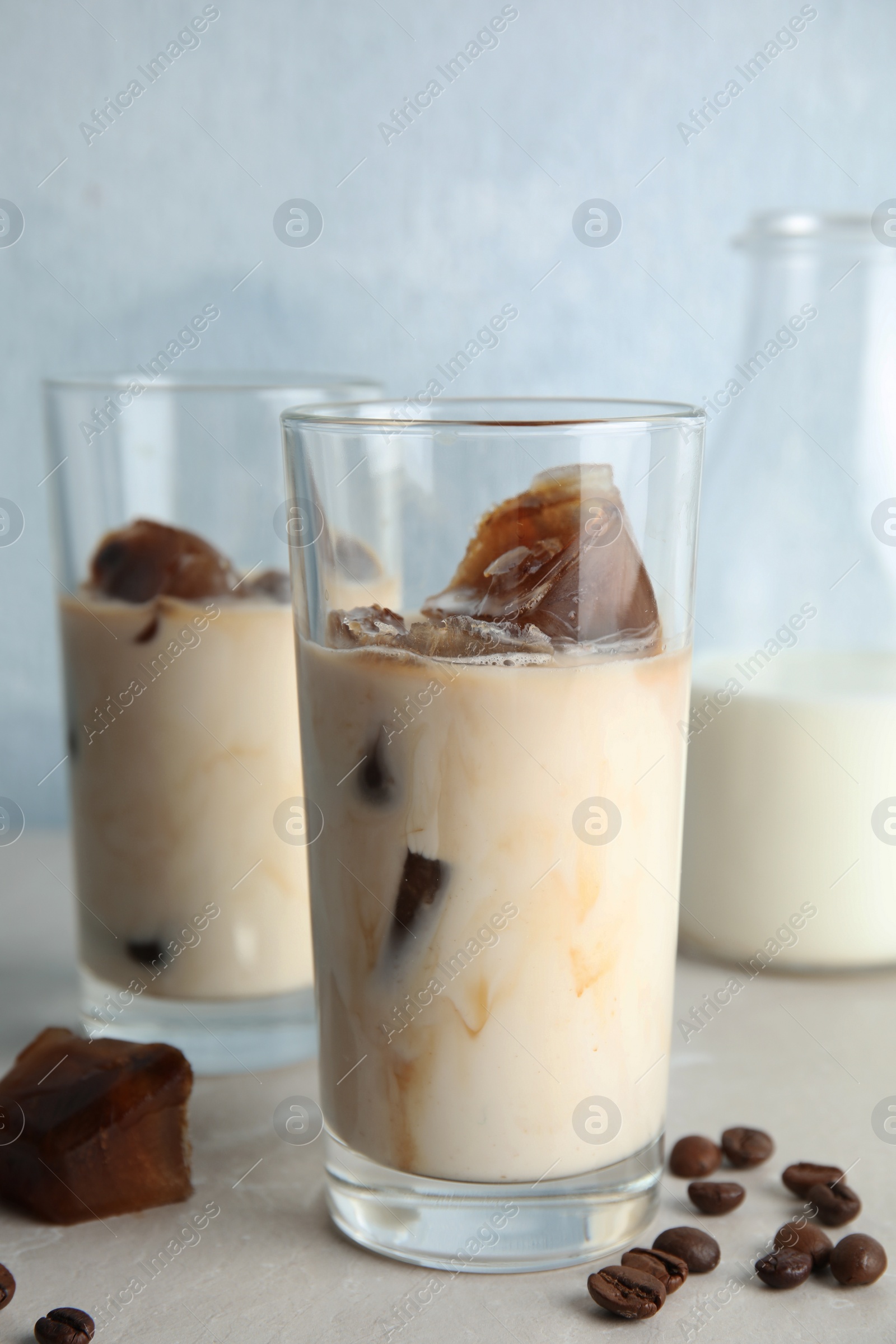 Photo of Glasses of milk with coffee ice cubes and beans on table against color background