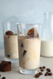 Glasses of milk with coffee ice cubes and beans on table against color background