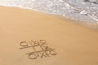 Photo of Tic tac toe game drawn on sand near sea, space for text