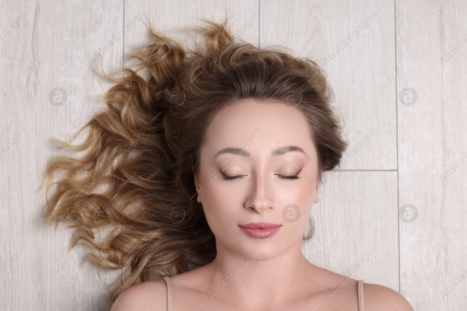 Photo of Portrait of beautiful woman with closed eyes on wooden floor, top view