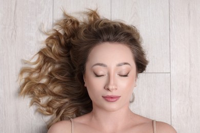 Portrait of beautiful woman with closed eyes on wooden floor, top view