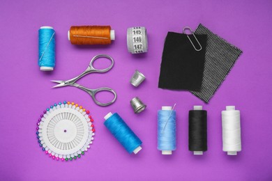 Photo of Flat lay composition with thimbles and different sewing tools on purple background