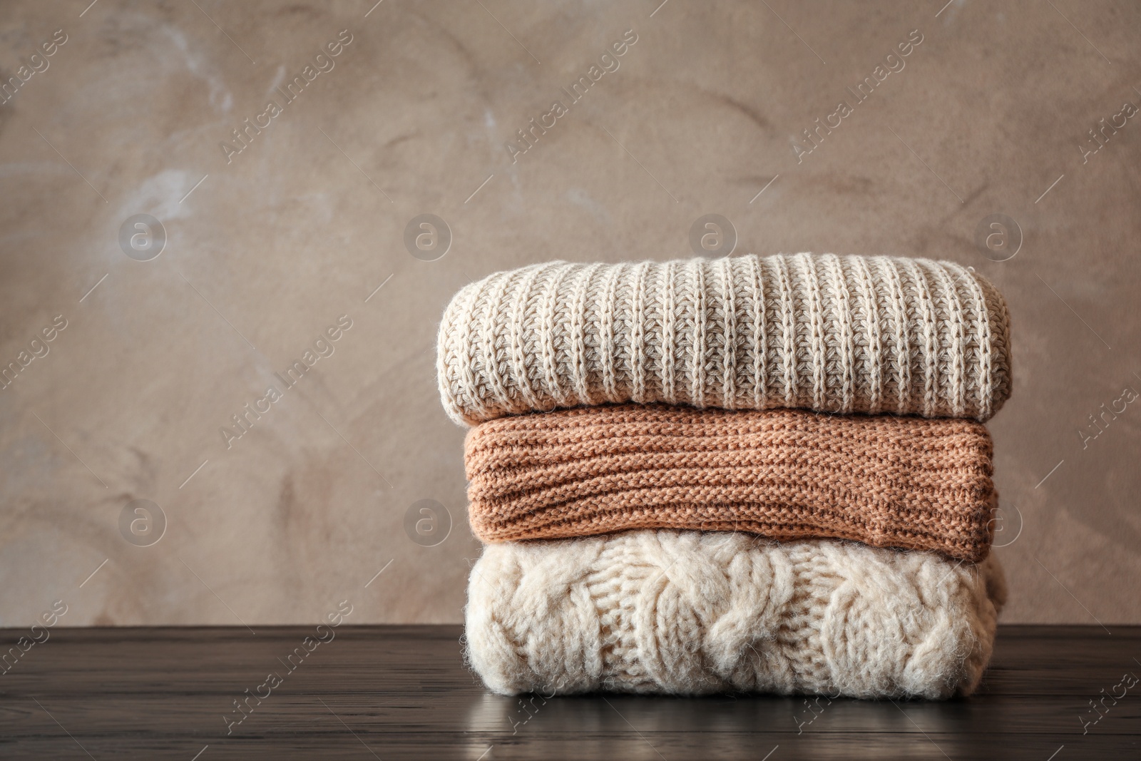 Photo of Stack of folded knitted sweaters on table. Space for text