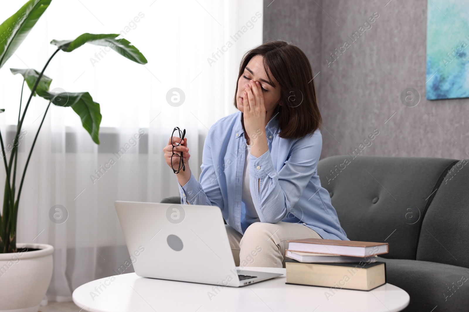 Photo of Overwhelmed woman with glasses sitting on sofa indoors