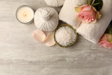 Flat lay composition with spa products, roses and burning candle on grey textured table. Space for text