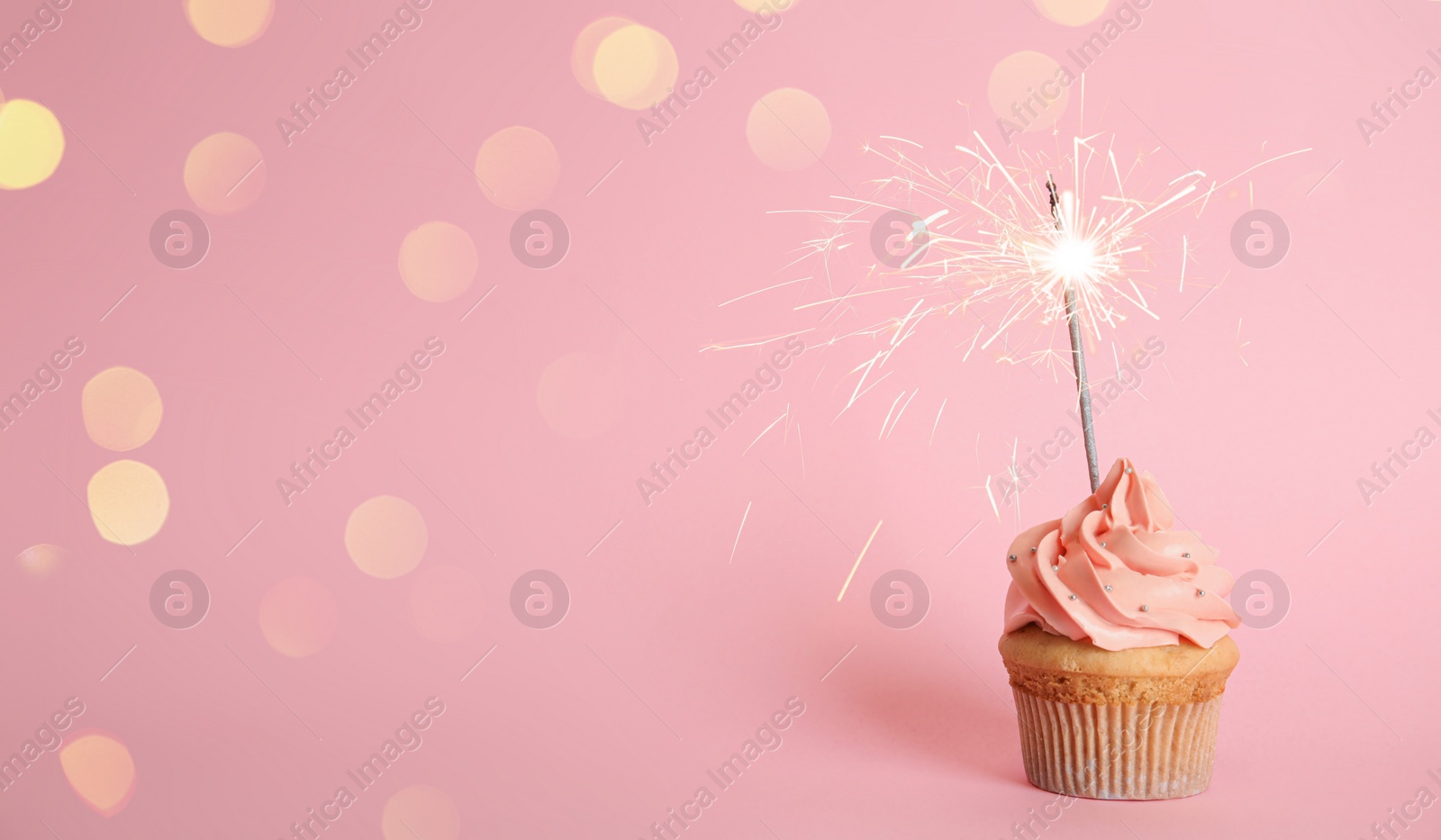 Image of Birthday cupcake with sparkler on pink background. Space for text