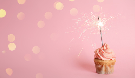 Birthday cupcake with sparkler on pink background. Space for text