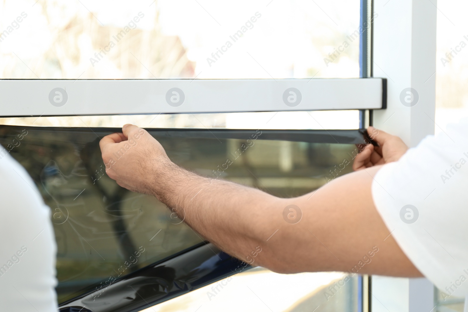 Photo of Professional worker tinting window with foil indoors, closeup