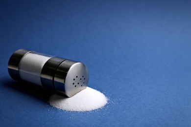 Photo of Scattered salt and shaker on blue background, closeup. Space for text