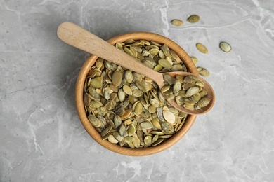 Photo of Bowl and spoon of raw pumpkin seeds on light grey marble table, top view