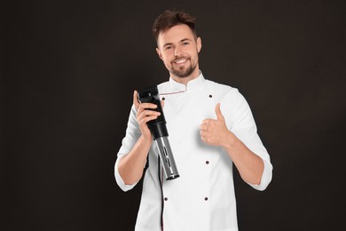 Photo of Smiling chef holding sous vide cooker and showing thumb up on black background