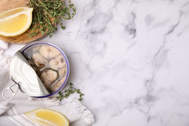 Photo of Open tin can with mackerel chunks, lemon and thyme on white marble table, flat lay. Space for text