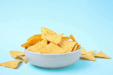 Photo of Bowl with tasty Mexican nachos chips on light blue background, space for text