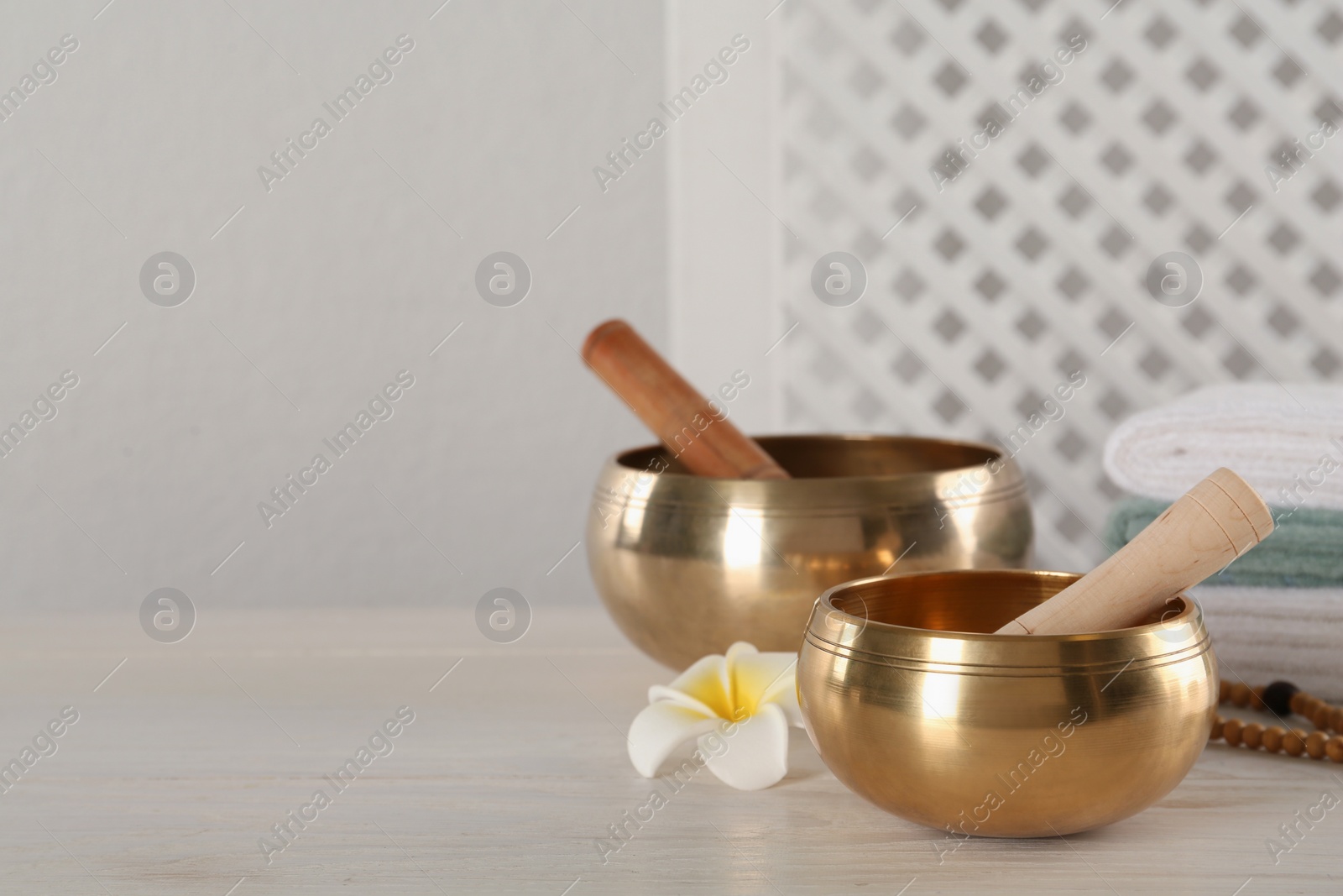 Photo of Golden singing bowls, mallets and flower on white wooden table, space for text