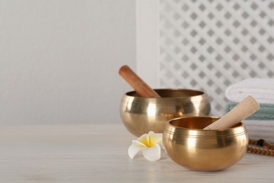 Photo of Golden singing bowls, mallets and flower on white wooden table, space for text