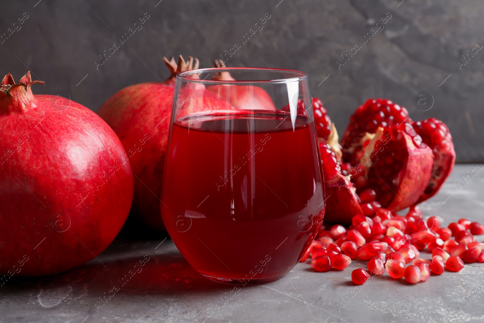 Photo of Glass of pomegranate juice and fresh fruits on table against grey background