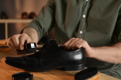 Man taking professional care of black leather shoe in workshop, closeup