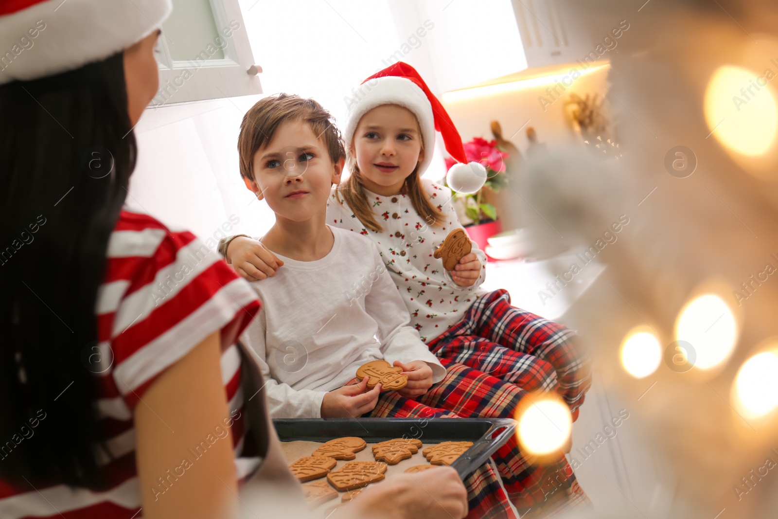 Photo of Mother giving her cute little children freshly baked Christmas cookies in kitchen