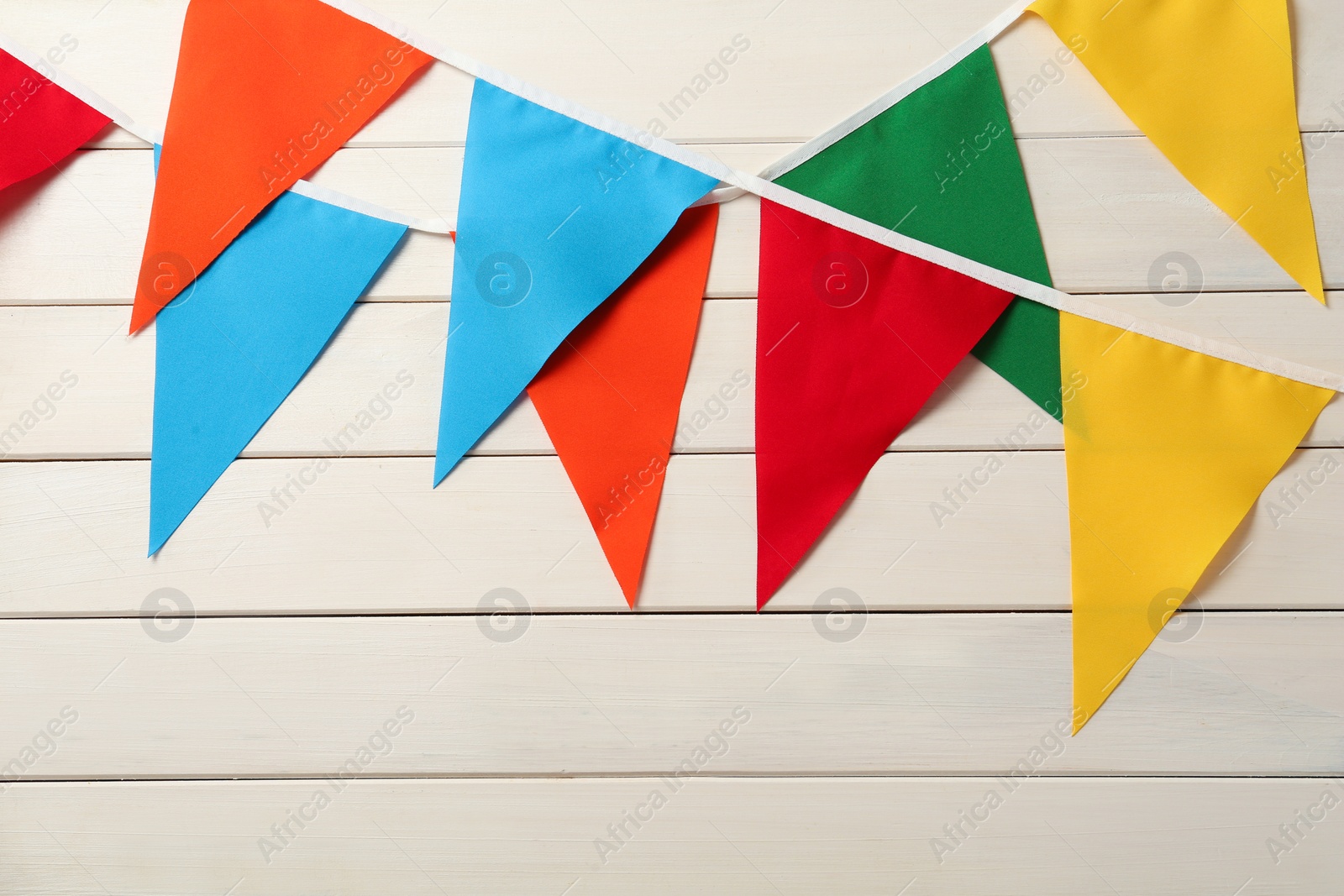 Photo of Buntings with colorful triangular flags hanging on white wooden wall. Festive decor