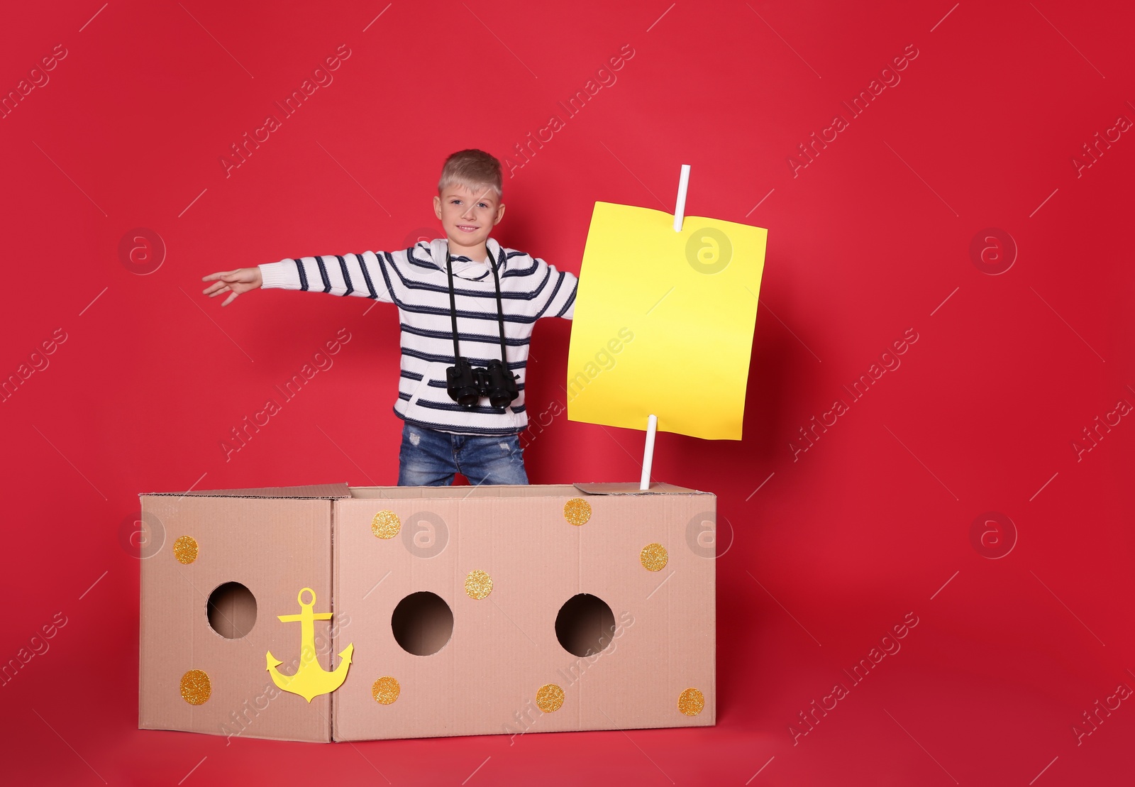 Photo of Little child playing with ship made of cardboard box on red background