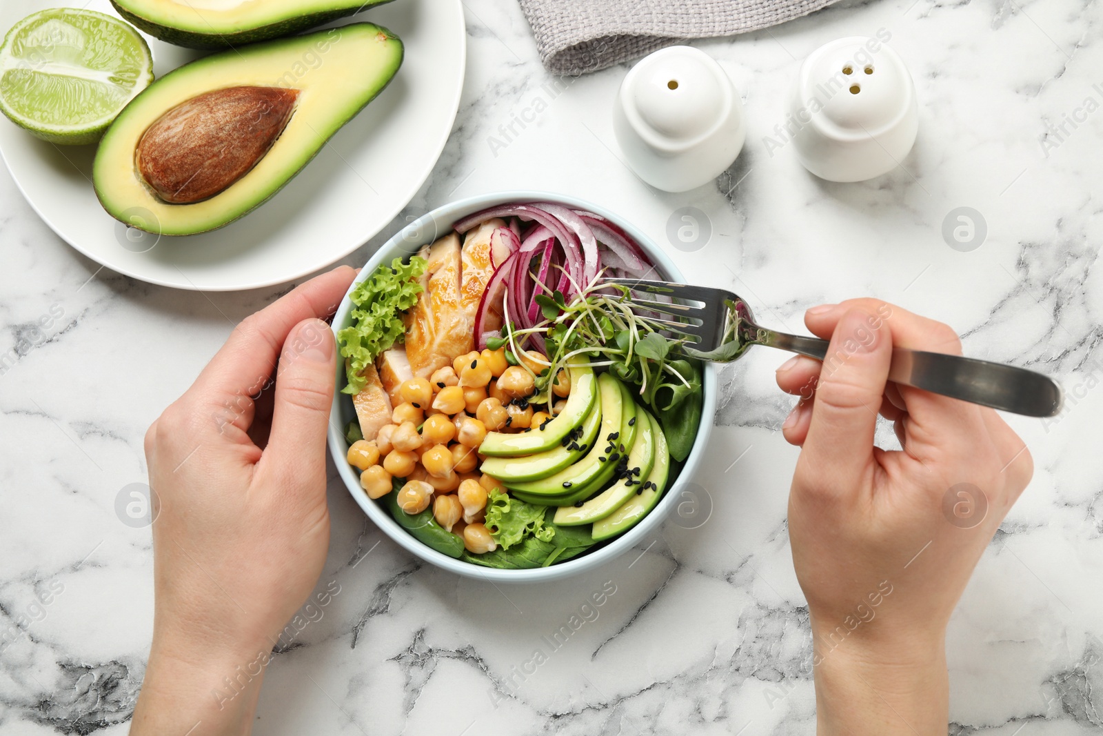 Photo of Woman eating delicious avocado salad with chickpea at white marble table, top view