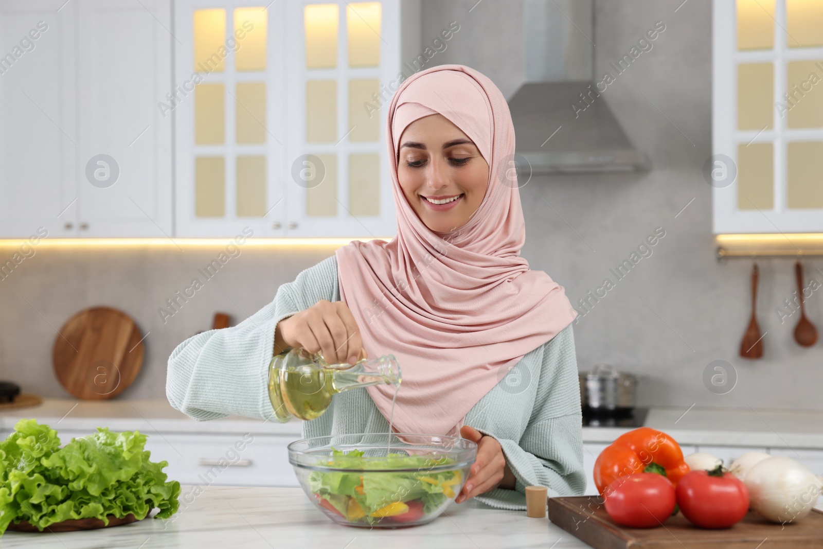 Photo of Muslim woman making delicious salad with vegetables at white table in kitchen