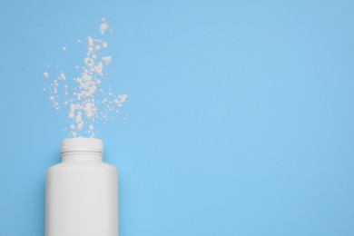Photo of Bottle and scattered dusting powder on light blue background, top view with space for text. Baby cosmetic product