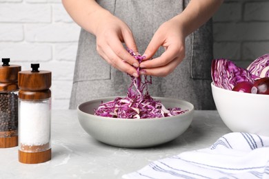Photo of Woman holding shredded fresh red cabbage at grey marble table, closeup