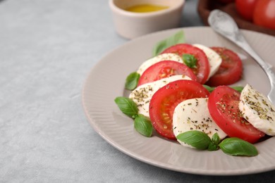 Photo of Delicious Caprese salad with tomatoes, mozzarella, basil and spices on light grey table, closeup