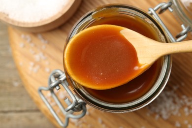 Photo of Jar and spoon with tasty salted caramel on table, top view