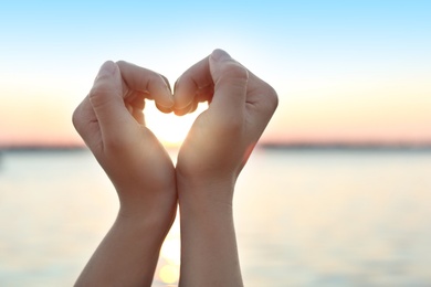 Photo of Woman making heart with hands outdoors, closeup
