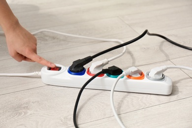 Photo of Woman pressing power button of extension cord on floor, closeup. Electrician's professional equipment