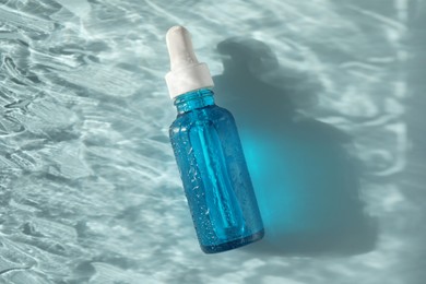 Wet bottle of cosmetic serum on light blue background, top view