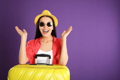 Beautiful woman with suitcase for summer trip on purple background. Vacation travel