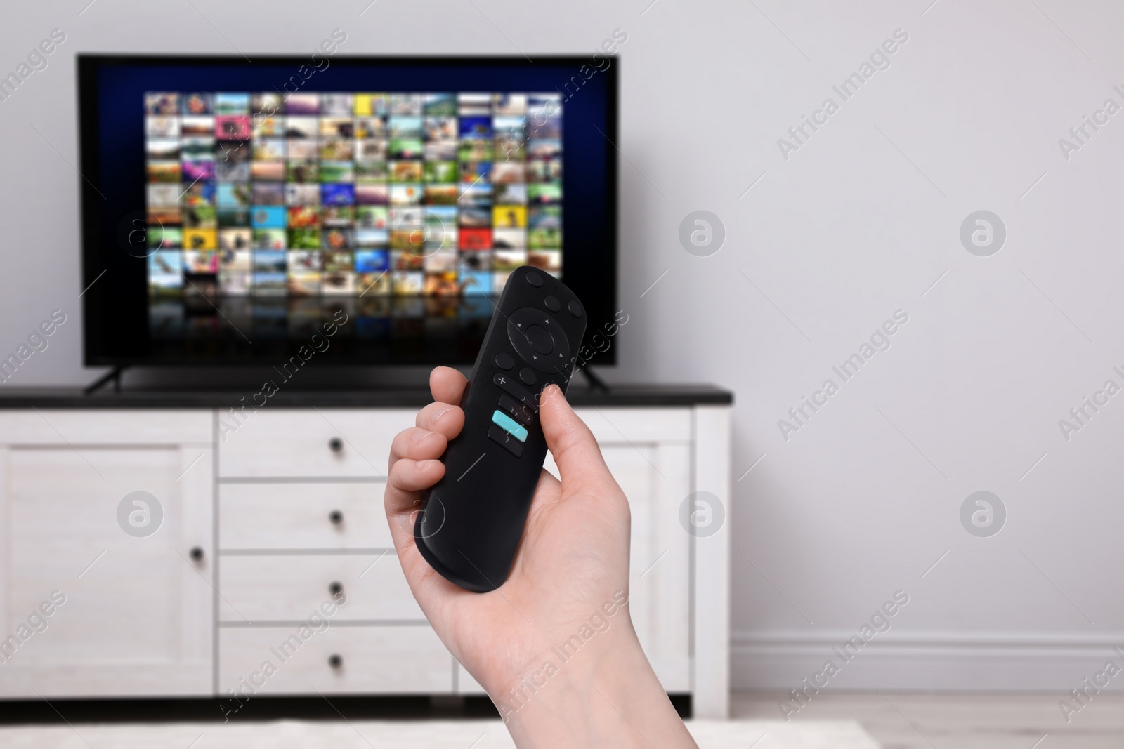 Image of Woman with remote control changing channels while watching TV at home, closeup